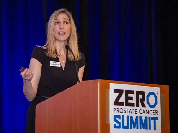 A blonde woman in a black dress behind the podium at Summit