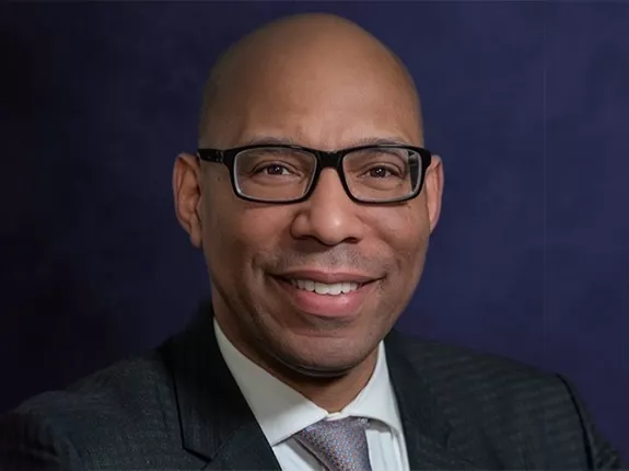 Black man wearing glasses and a black suit posing for headshot