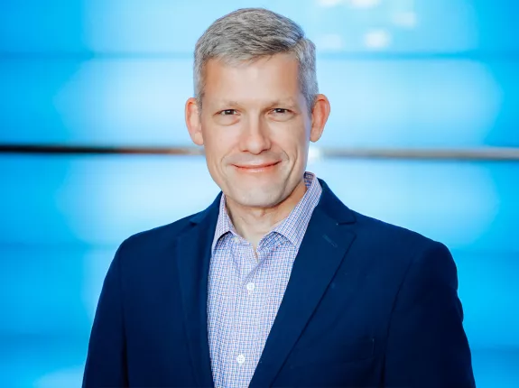 A white man with gray hair wearing a blue suit against a blue background