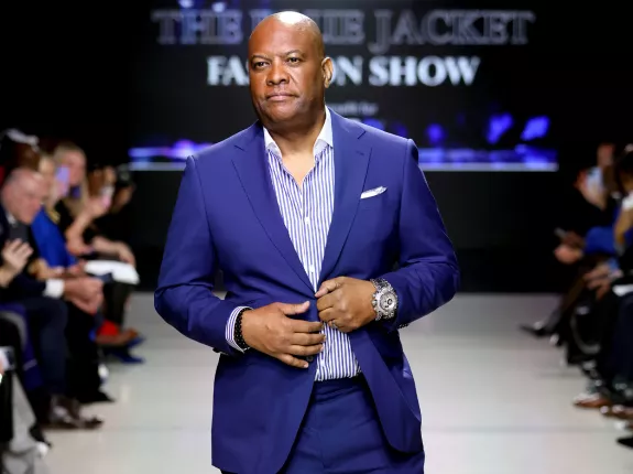 A Black man wearing a blue suit on the runway of the Blue Jacket Fashion Show