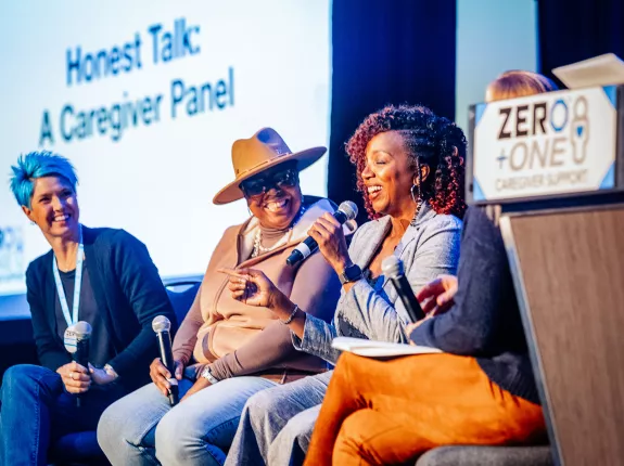 A woman with blue hair, a Black woman with a hat, and another Black woman sitting on stage for a panel discussion