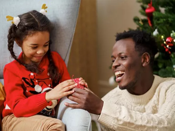 A middle ages Black man and a young girl in front of a Christmas tree