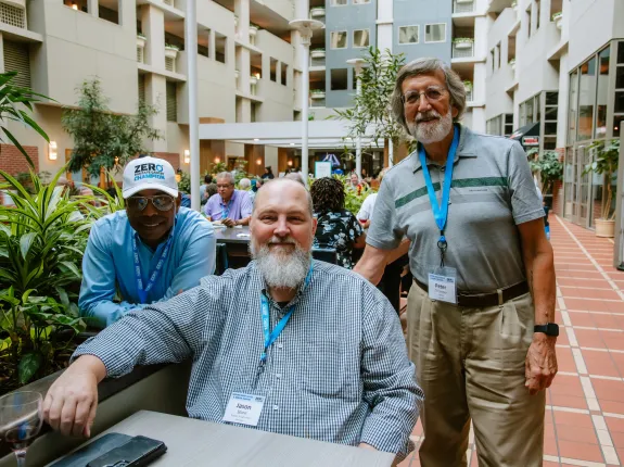 Three men sit together in a courtyard and smile at the camera.
