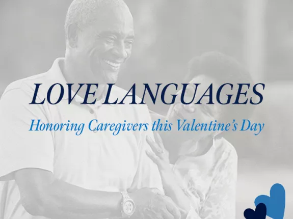 A promotional banner for ZERO Prostate Cancer featuring the text "LOVE LANGUAGES" in dark blue capital letters, with "Honoring Caregivers this Valentine's Day" in light blue script below. The background shows a soft, grayscale image of what appears to be a caregiver interaction. The ZERO Prostate Cancer logo appears in the bottom left corner, and two hearts (one dark blue, one light blue) are positioned in the bottom right corner.