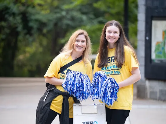 Two volunteers holding poms poms wearing yellow ZERO volunteer shirts