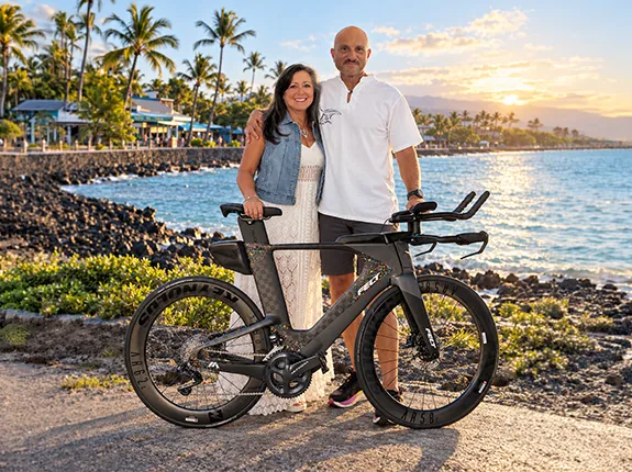 Peter Crescenti and wife standing by bike in front of water and lake and palm trees