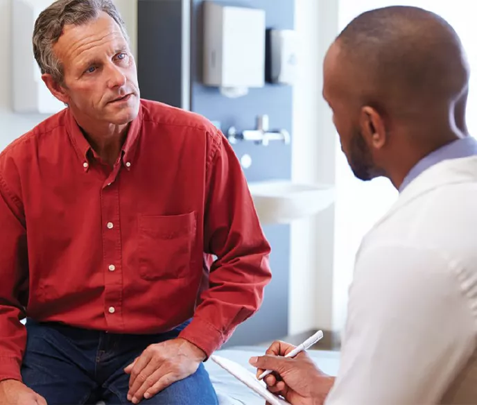 A white man in a red shirt sitting across from a Black doctor