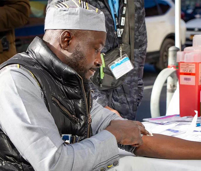 A Black man sitting at a table holding his arm after receiving a blood draw for PSA test