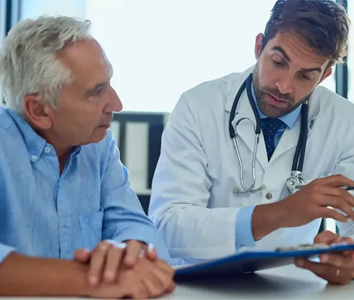 A man sitting with his doctor who is holding a clipboard