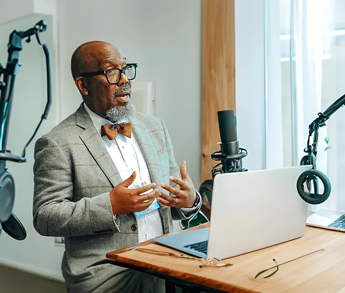 Dr. Reggie Tucker-Seely in front of a computer and microphones 