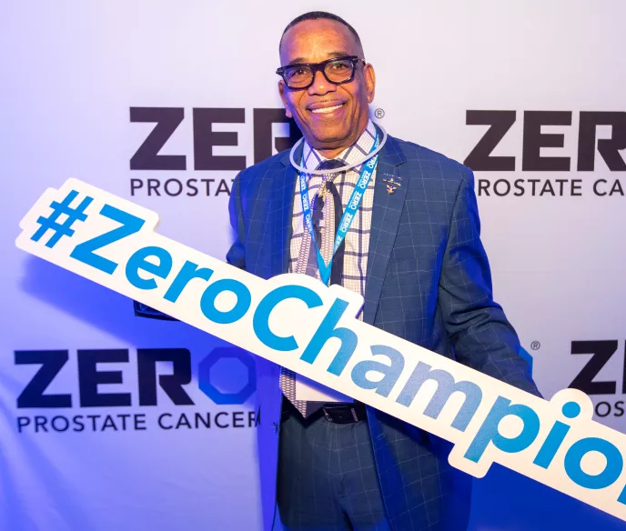 African American man in a suit holding a ZERO Champion sign