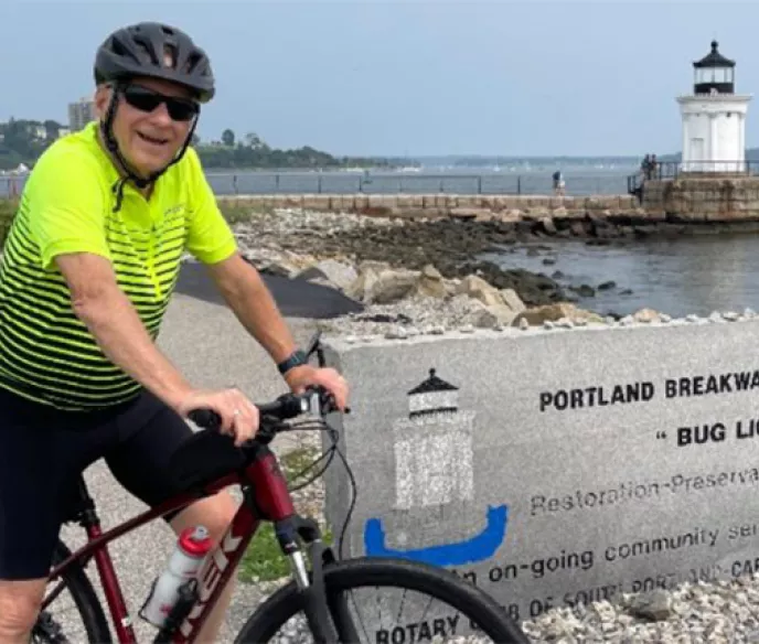 Champion Larry Langmore on a bicycle wearing a neon green bike jersey stopped in front of a lighthouse