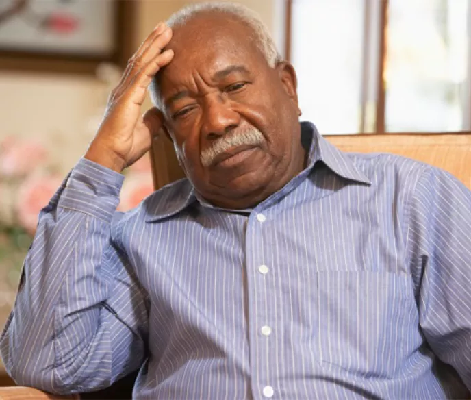 An older black man with his head on his hand as he slumps in a chair
