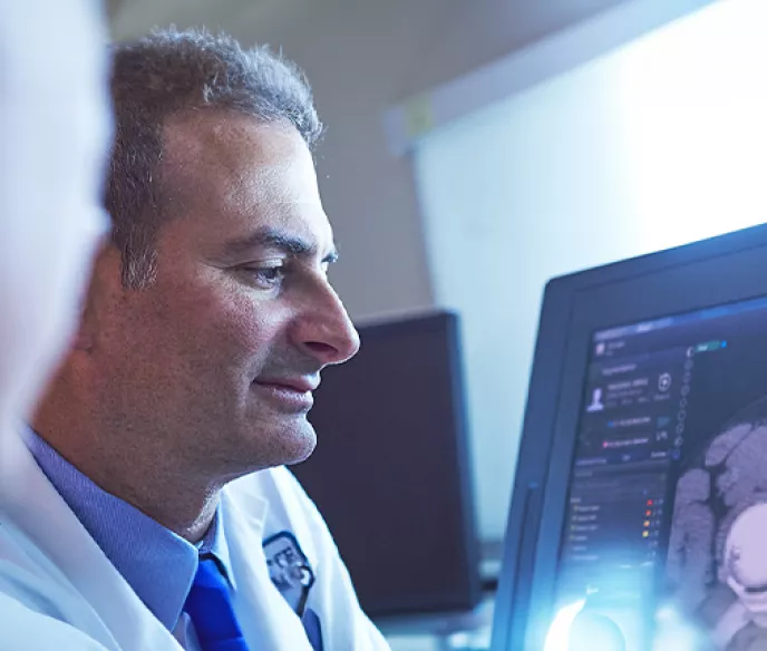 A man in a doctor's coat looking and radiographic imaging of a prostate on a computer