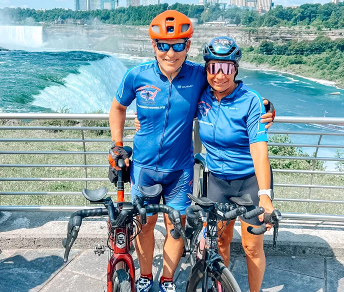 Scott and Katy Freitag in cycling gear standing with their bicycles on a bridge overlooking a dam
