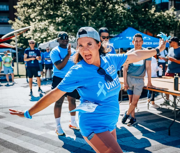 A woman with a backwards hat wearing a Run/Walk shirt standing with her arms out in a silly position