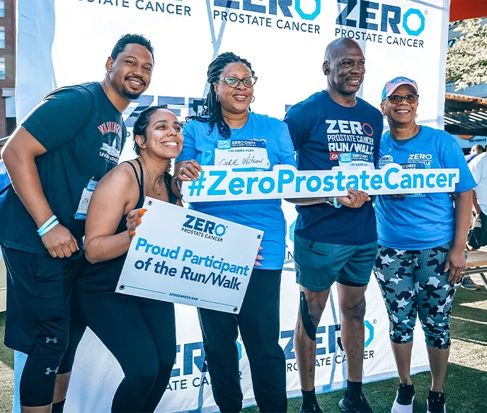 A group of adults at a Run/Walk standing in front of the step-and-repeat holding signs for ZERO