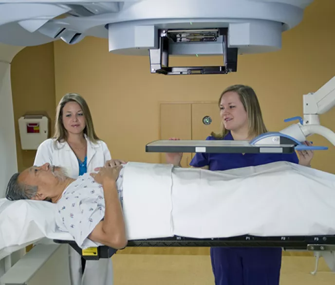 Stock photo of man lying down for test surrounded by two female healthcare professionals