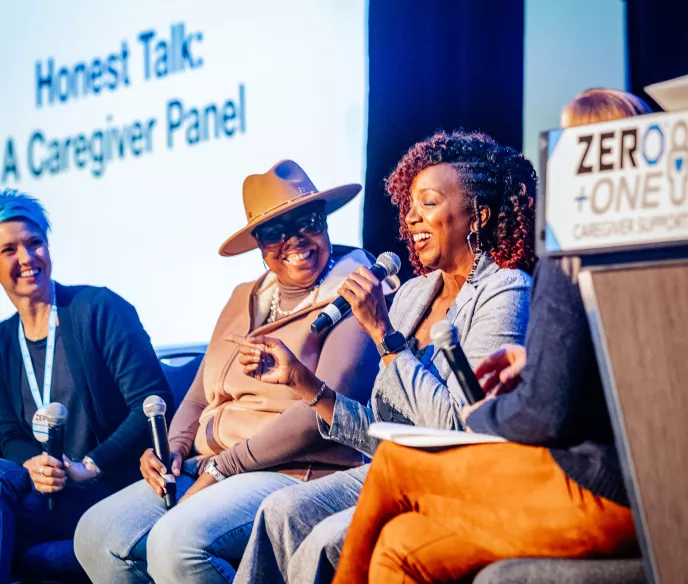 A woman with blue hair, a Black woman with a hat, and another Black woman sitting on stage for a panel discussion