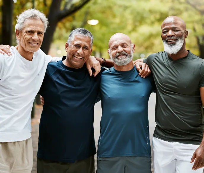 Four men standing with arms around each other shoulder to shoulder smiling