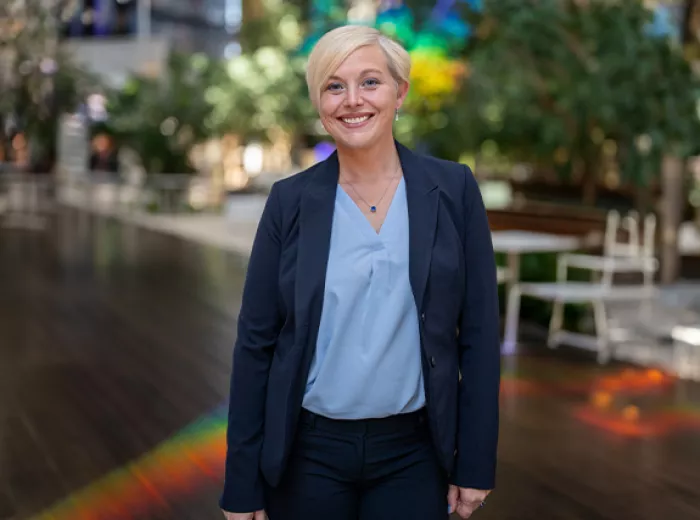ZERO President & CEO, Courtney Bugler, standing in a room with wood floors, trees in the back, and a lighting casting a rainbow on the ground behind her