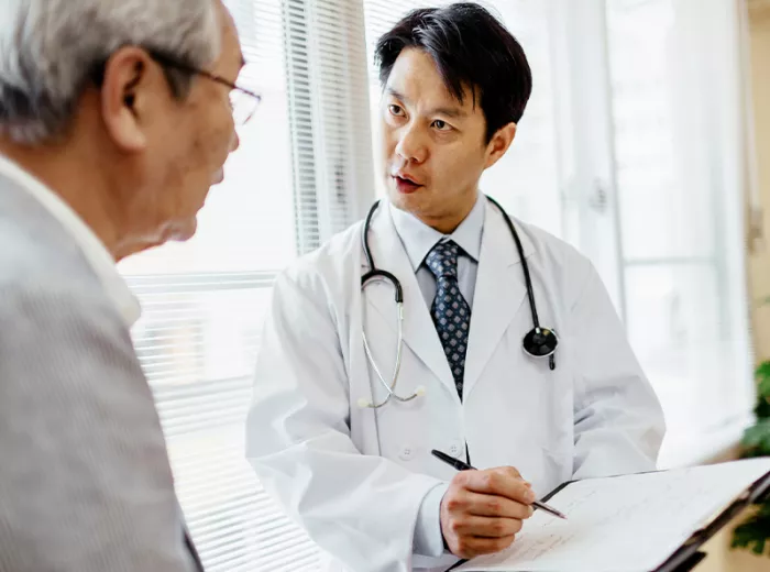 An asian doctor sitting with an older male patient