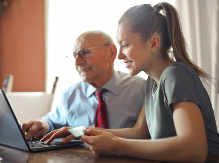 A younger woman helping an elderly man by using a laptop