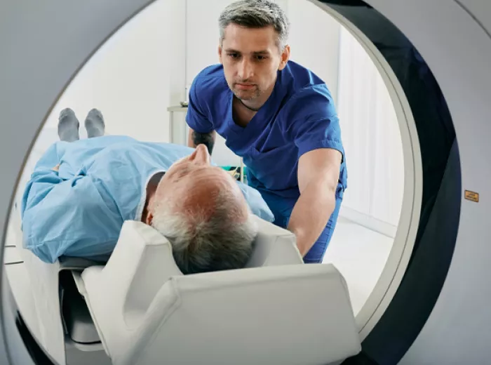 Healthcare worker assisting man into an imaging machine