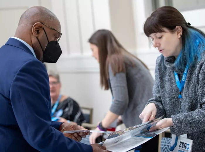 A woman with blue hair highlights sharing reading materials with an African American man in a suit