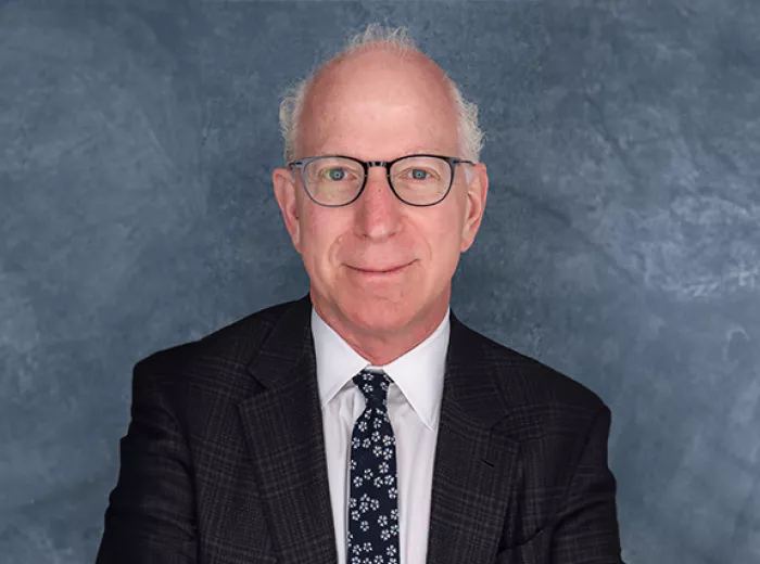 White man in black suit and tie against a blue portrait background, Dr. Howard. Sandler