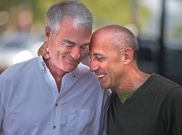 Two older men smiling with their heads pressed together 