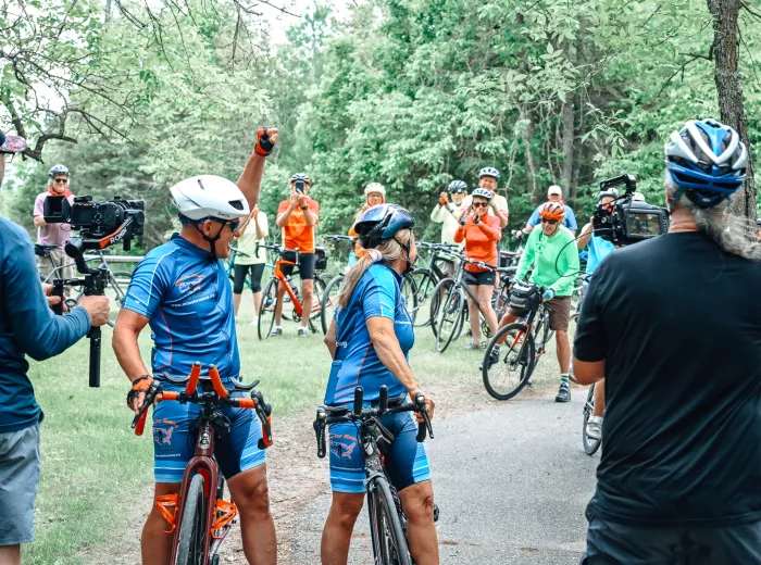 A couple, Scott and Katy Freitag, on their bicycles and facing a crowd who is cheering them on from behind