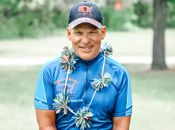 A man, Scott Freitag, wearing a blue cycling jersey and hat that says Miles for Money