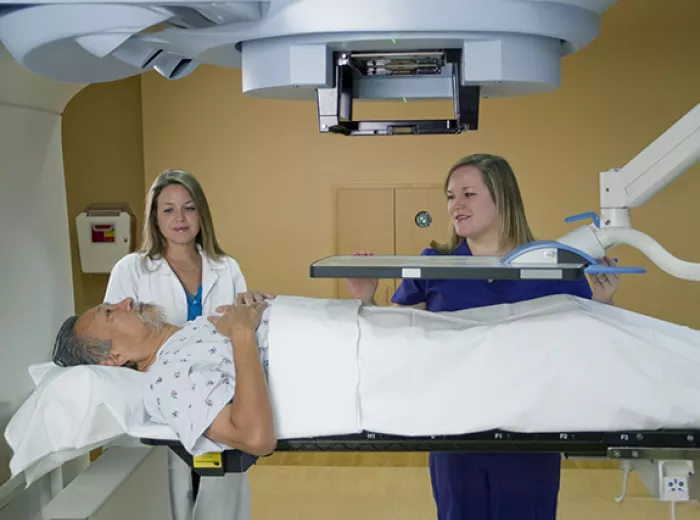 Stock photo of man lying down for test surrounded by two female healthcare professionals