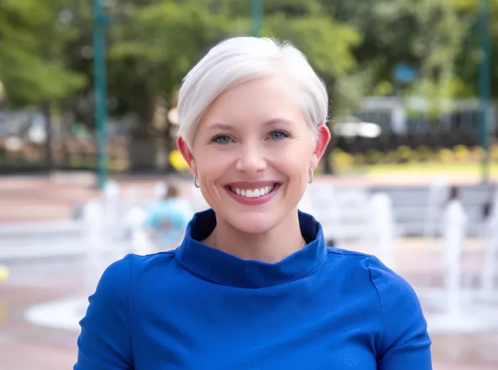 Courtney Bugler in a blue dress standing in front of water fountains