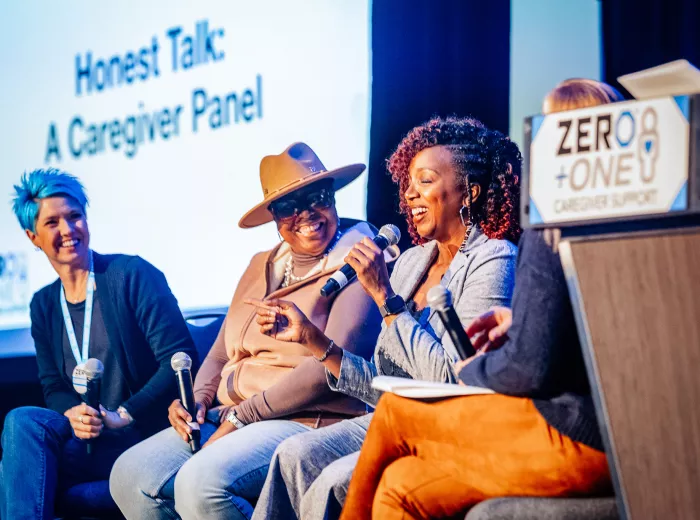 A woman with blue hair, a Black woman with a hat, and another Black woman sitting on stage for a panel discussion