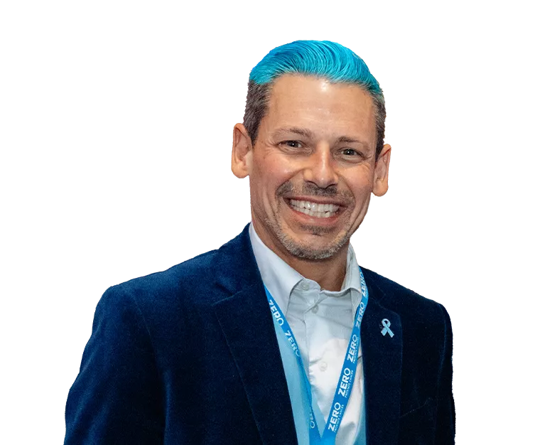 A man with blue hair wearing a suit and a blue ZERO lanyard with a huge smile