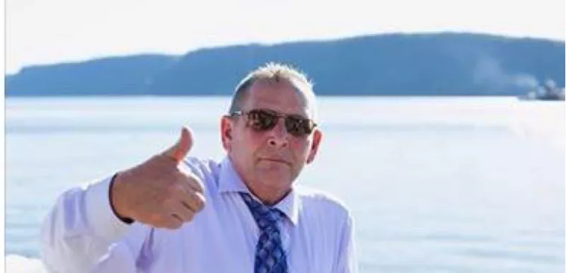 David Zarach giving a thumbs up while leaning on a railing by a sunny body of water