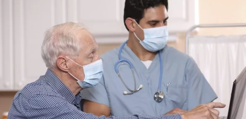 Doctor discusses results with patient on laptop while wearing masks