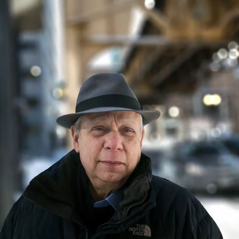 Man in gray fedora wearing north face jacket under blurred out train tracks