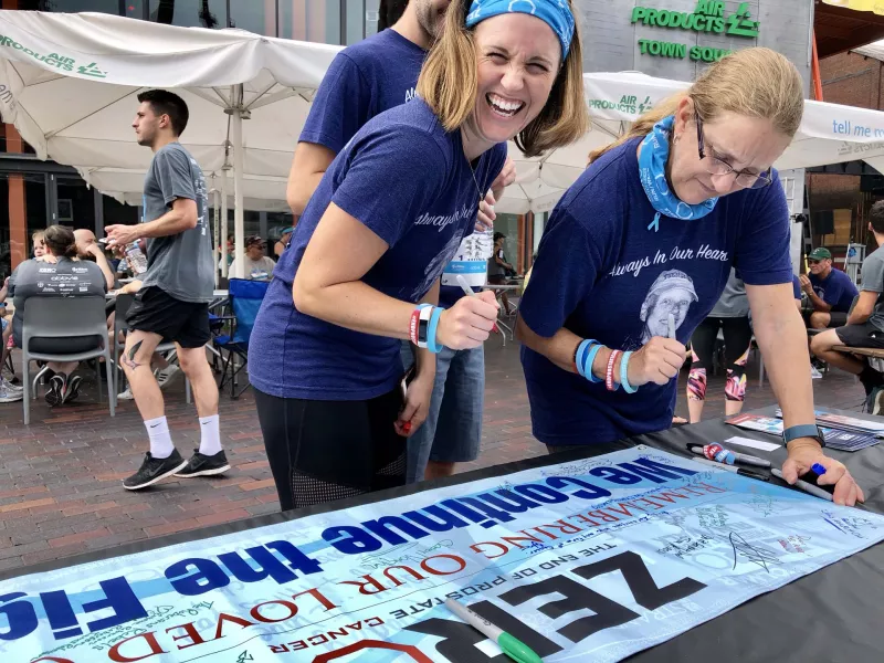 Two women wearing memorial shirts sign a remembrance banner for ZERO