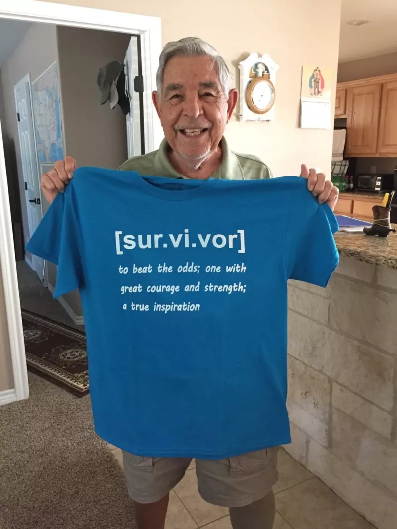 Father holding up a shirt saying survivor definition to beat the odds; one with great courage and strength; a true insipration