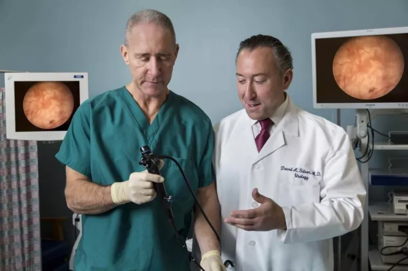Dr. David Silver at work with a partner holding a scope showing images of a procedure in the background