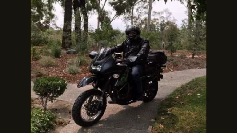 Man on his motorcycle fully suited up in all black sitting on the sidewalk