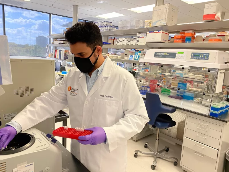 Jose Gutierrez wearing full lab gear in the lab holding a tray of specimens