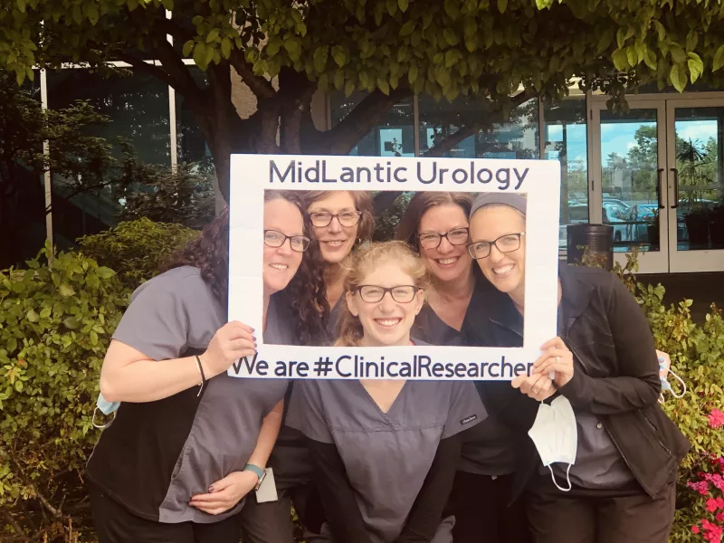 Professionals in scrubs holding up a selfie cutout that reads MidLantic urology We are #ClinicalReserher