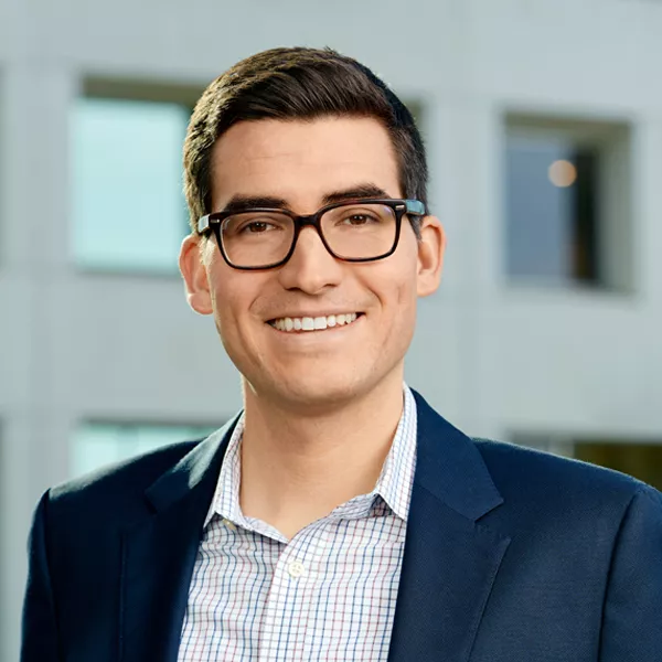 White male smiling with glasses in front of office building