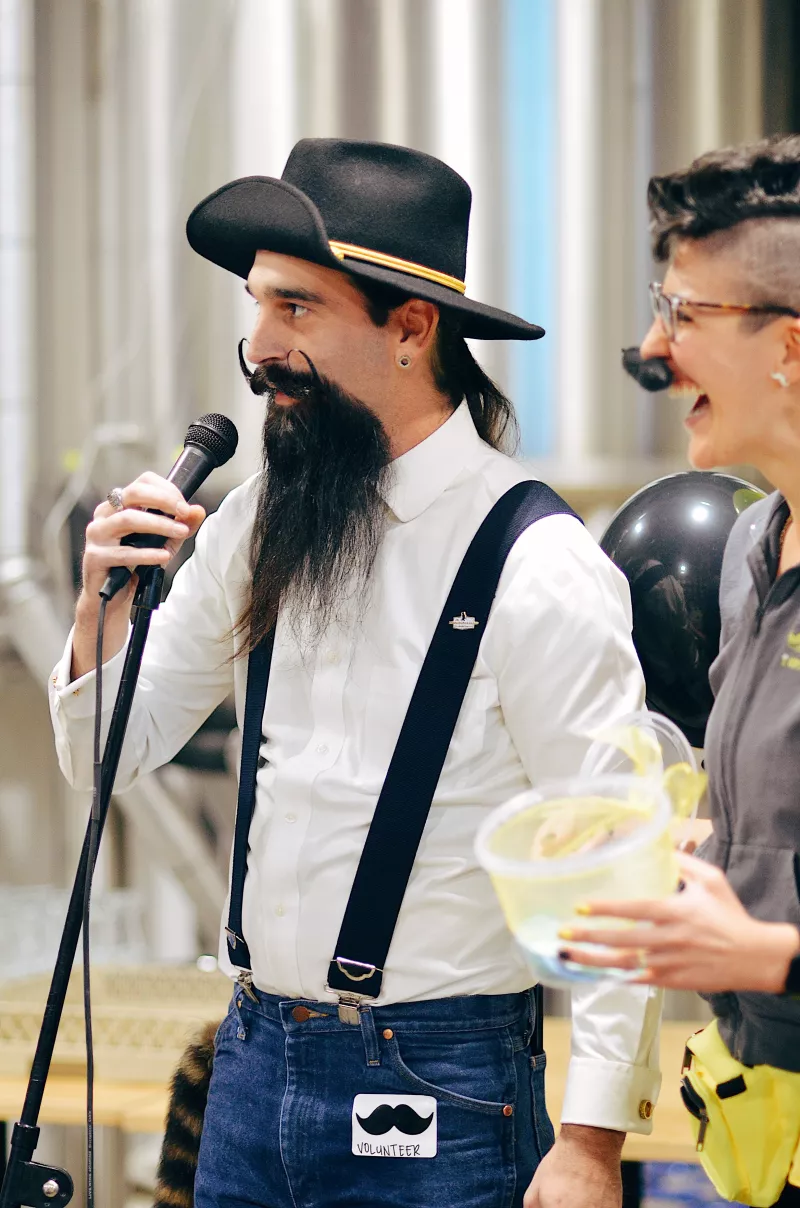 A man with long beard and handlebar mustache wearing suspenders jeans and a fancy hat