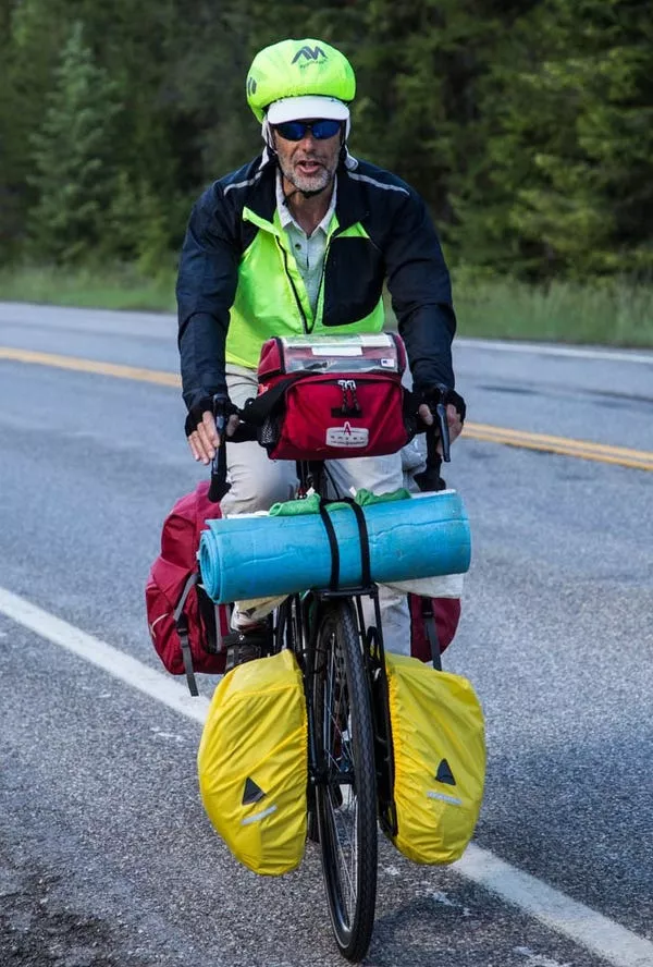 Man on his journey cross country with bicycle packed full of bags, a yoga mat, safety gear and more