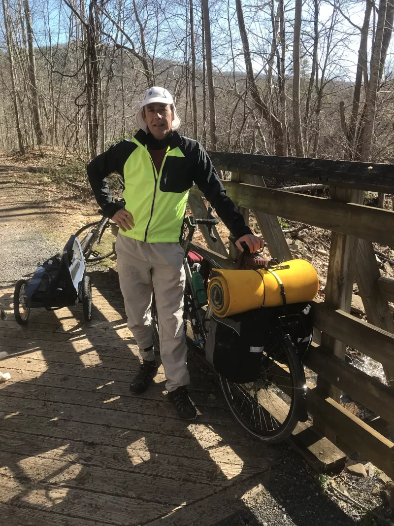 Man stands in front of his bicycle with full gear prepared to trek cross-country